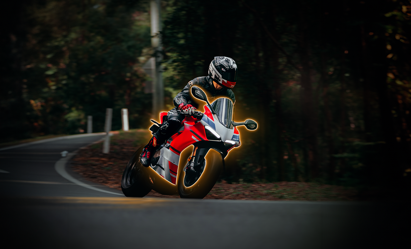 Image of a person on a motorcycle with a yellow glow surround, driving on a curved bend road at dusk in a forest setting